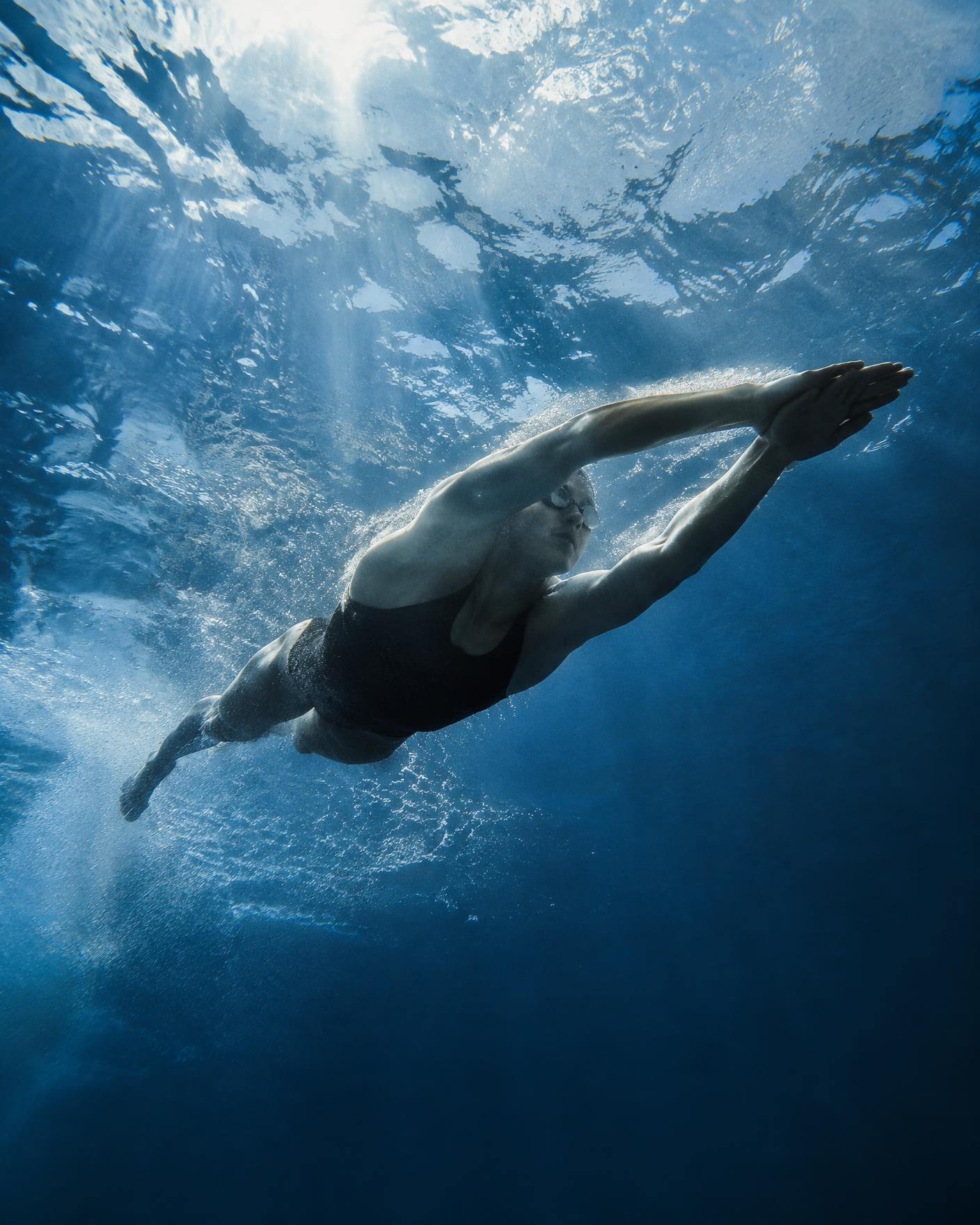 Swimmer gliding through deep blue water seen from below